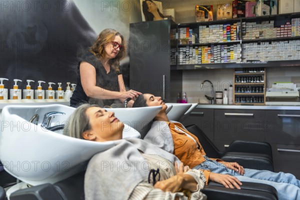 Hairdresser performing a relaxing hair wash for two women at a modern salon, creating a pampering experience with steam rising from the basins, emphasizing beauty treatment and self care
