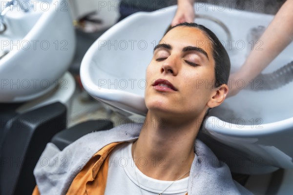 Woman closing her eyes while relaxing and receiving a professional hair wash and steam treatment at a modern hair salon, enjoying the pampering beauty experience