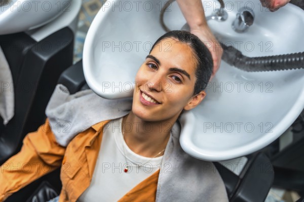 Young woman smiling and relaxing as a hairdresser shampoos and rinses her hair at a professional salon sink, enjoying pampering, scalp massage and beauty care