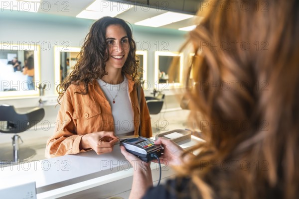 Smiling woman paying with a contactless credit card at a modern hair salon reception, completing a beauty service transaction at the checkout counter with ease and satisfaction