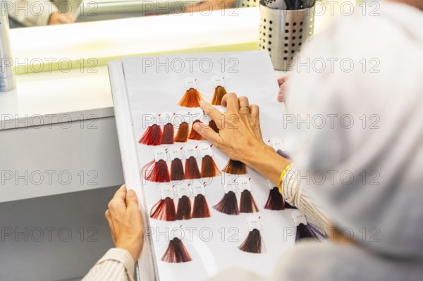 Client selecting desired hair dye shade from a detailed color chart while sitting in a hair salon, making a beauty decision for a new look or hair treatment