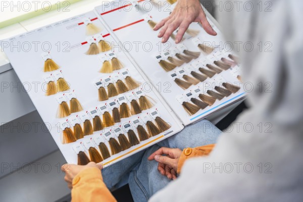 Client and hairdresser comparing color chart swatches in salon, discussing shades and tones to choose a new look during a consultation for hair color transformation