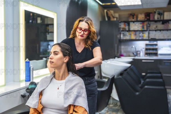 Hairstylist working through a young woman's damp brunette hair in a bright modern salon, preparing her for treatment or styling with focused, professional care and pampering