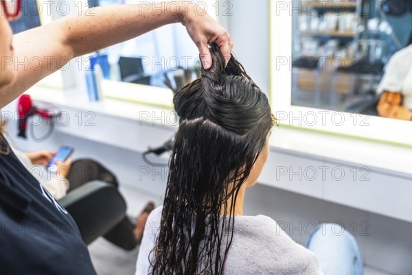 Hairdresser holding sections of wet hair on a woman's head in a bright salon, preparing for a haircut or styling session, focusing on professional beauty treatment