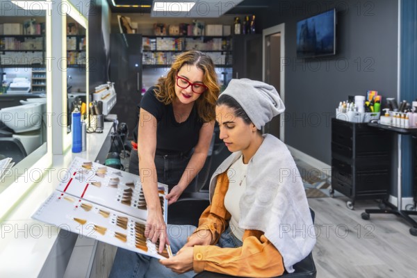 Professional hairstylist advising female client during a beauty consultation, pointing at hair dye chart to choose the perfect shade for personalized hair color and styling choices