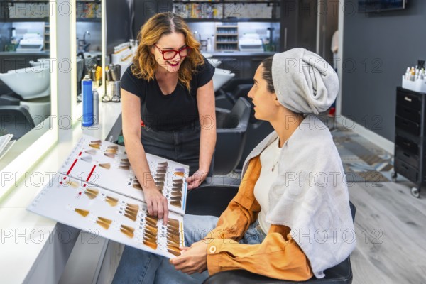 Hairdresser and female client compare a color swatch chart during a friendly consultation in a modern salon, choosing hair dye options with smiles and professional care