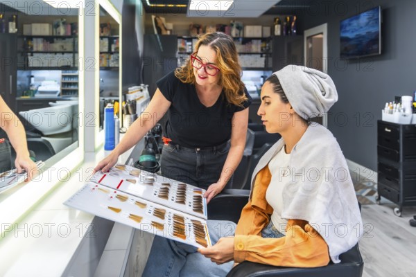 Professional hairstylist assisting a young woman in choosing the perfect hair dye shade from a color swatch book during a consultation at a modern hair salon