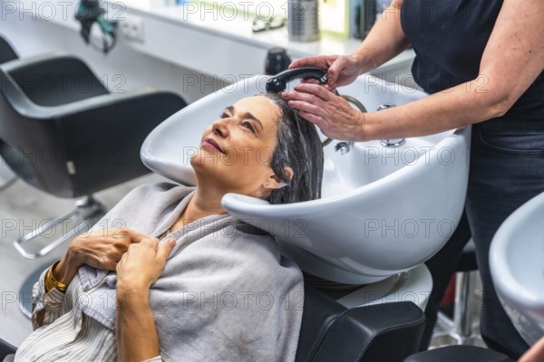 Hairdresser washing a smiling woman's hair at a modern salon, creating a relaxing experience and focusing on self care, beauty, and pampering during a professional service