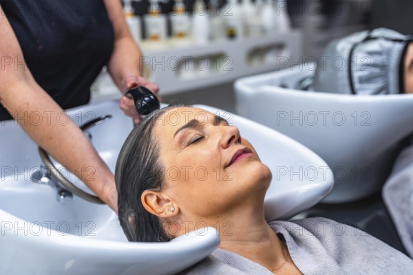 Woman with closed eyes relaxing during a hair wash service at a beauty salon, symbolizing self care, pampering, and professional treatment in a serene environment