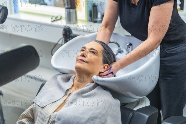 Senior woman smiling as a hairstylist gently washes her hair at a modern salon basin, enjoying a relaxing pampering treatment that promotes well being and confidence