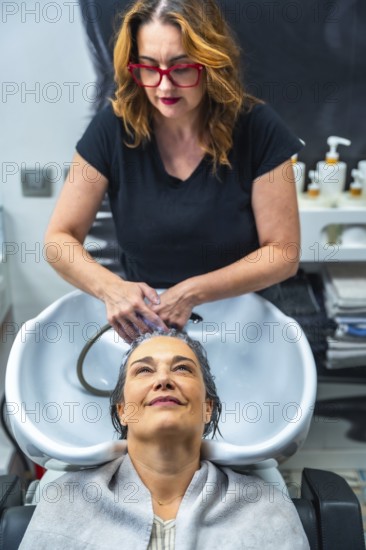Hair stylist washing a mature woman's hair at the shampoo sink, creating a moment of self care, relaxation, and beauty treatment in a modern hair salon environment