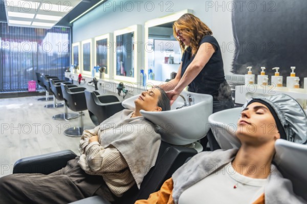 Hairdresser washing client's hair at a modern salon basin, two women enjoying a relaxing, professional hair treatment and pampering self care experience in a bright interior