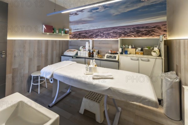 Beauty salon treatment room offering services for skin care, massage, and wellness, featuring a comfortable bed, professional equipment, and a calming ocean themed wall art