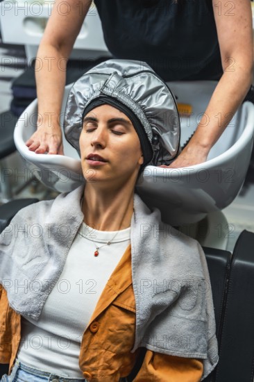Relaxing woman with eyes closed wearing a heat cap during a professional hair treatment at a modern hair salon, enjoying a pampering beauty experience