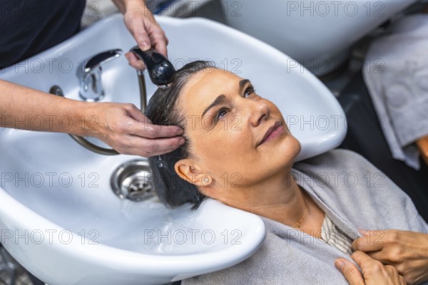 Senior woman smiling as a professional hairdresser washes and massages her hair at a salon sink, enjoying a relaxing shampoo treatment and pampering salon experience