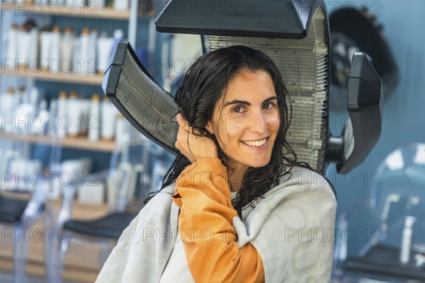 Woman relaxes under a salon hair dryer during a pampering hair treatment, smiling with wet hair as she enjoys beauty, self care and professional styling for a fresh look