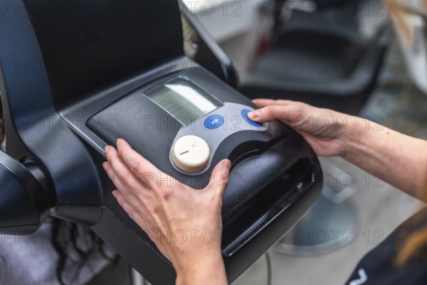 Hairdresser hands adjusting controls on a modern hair treatment machine, delivering professional beauty services in a hair salon setting with a client receiving care