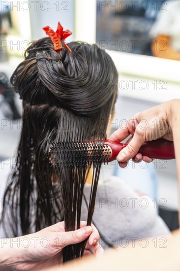 Hairdresser performing a hair styling service on a female client, brushing her wet dark hair after washing and preparing it for further treatment in a beauty salon