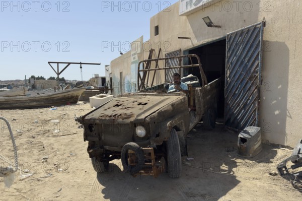 Rusty and almost broken car in front of garage or workshop, Oman