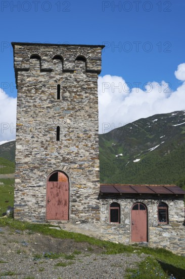 Old stone tower and small building against a mountain backdrop under a deep blue sky, defensive towers, Ushguli, Upper Svaneti, Svaneti, Georgia