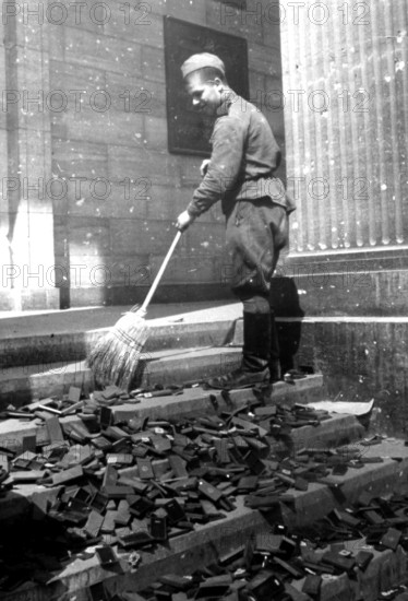 Soldier sweeping boxes of National Socialist medals from a staircase in the Reich Chancellery, early May 1945, Berlin, Germany