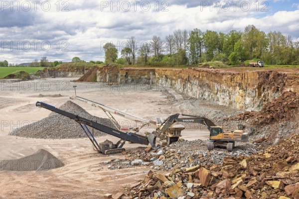 Open pit mining with an excavator at a stone crusher and a conveyor for loading stones