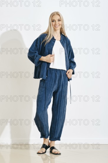 A woman stands in a bright indoor setting wearing a blue outfit made of light fabric. She smiles and poses confidently, highlighting her style. The background is simple with white walls