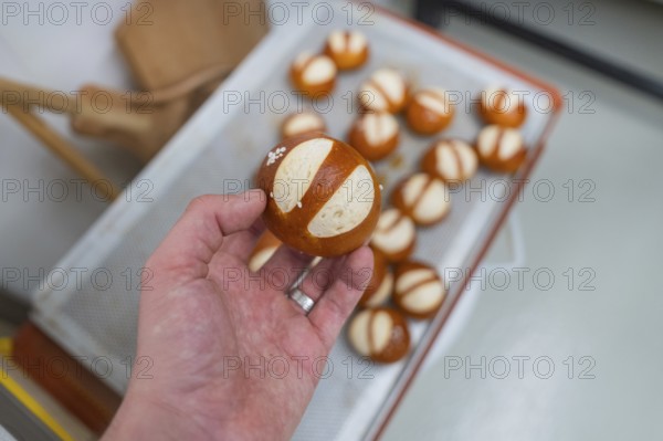 Hand holding a baked pretzel over a tray with other pretzels, bake rolls, Haselstaller Hof, Gechingen, Germany