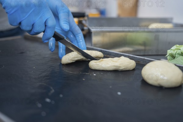 A baker shapes and cuts dough with a knife on a black surface, bake rolls, Haselstaller Hof, Gechingen, Germany