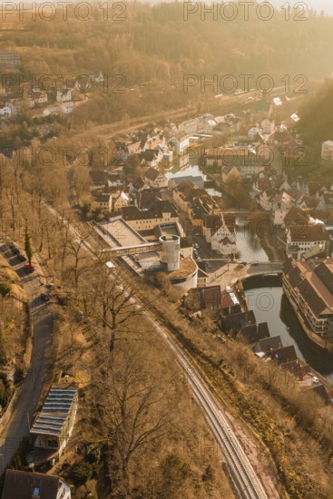 Aerial view of a village with tracks and river surrounded by trees in sunlight, test run on the new Hermann Hesse railway with Siemens Mireo Plus B trains, Calw, Germany