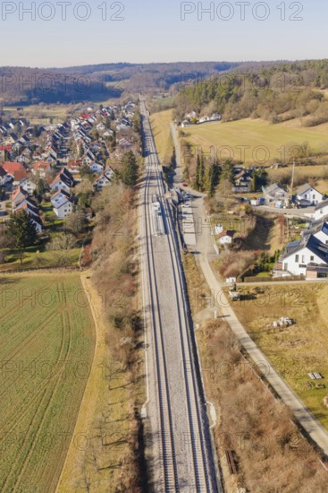 Aerial view of railroad tracks running through a rural area with houses and fields, test run on the new Hermann-Hesse railway with Siemens Mireo Plus B trains, Calw, Germany