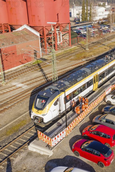 Close-up of a train at a station surrounded by industrial buildings, cars and several workers, test run on the new Hermann Hesse railway with Siemens Mireo Plus B trains, Calw, Germany