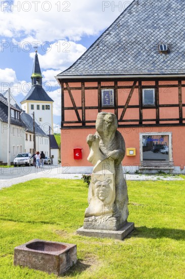 Sandstone figure bear with coat of arms on Bärenstein market square, church in the background, Altenberg, Eastern Ore Mountains, Saxony, Germany
