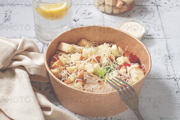Caesar salad in a paper container, take it on the way, with sauce and croutons, on the table, snack, natural light, no people
