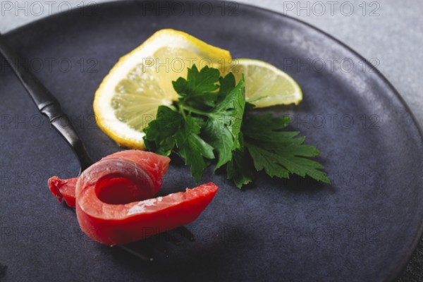 Chum salmon, cold smoked, on a fork, with lemon and parsley, top view, close-up, no people
