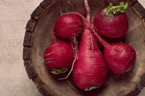 A collection of vibrant red radishes sits in a round wooden bowl, showcasing their natural texture and earthy tones against a softly colored background