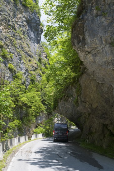 A black van passes a narrow road under a natural rock arch, camper, motorhome in a gorge on the Lajanuri River near Achara, Racha-Lechkhumi region and Lower Svaneti, Georgia