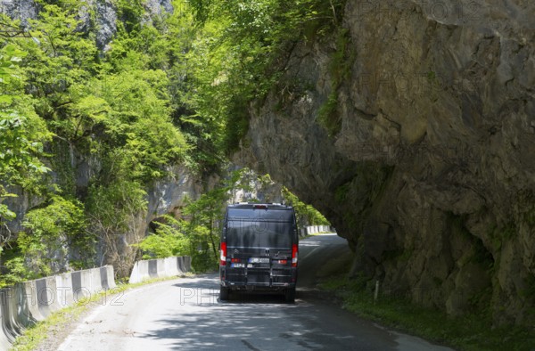 A black van drives on a narrow mountain road surrounded by lush greenery, camper, motorhome in a gorge on the Lajanuri river near Achara, Racha-Lechkhumi region and Lower Svaneti, Georgia