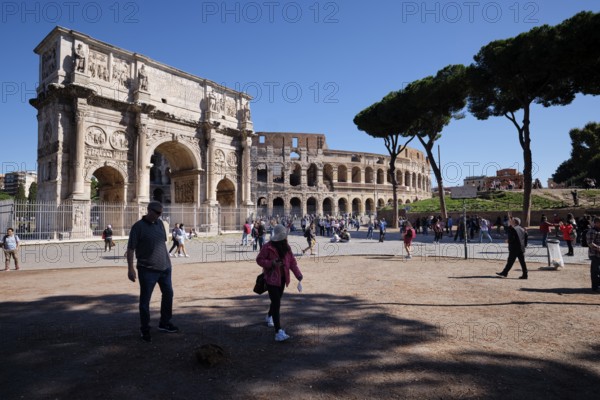 Tourists in front of the Colosseum and Arch of Constantine on a sunny day surrounded by trees, Rome, Lazio, Italy