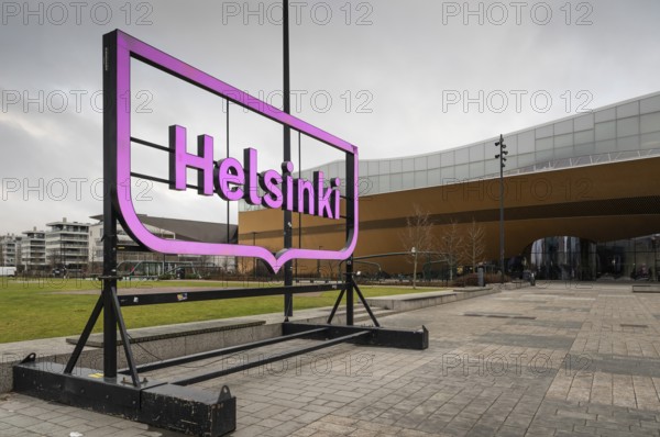 Large pink glowing Helsinki city logo, in front of Oodi Central Library and Cultural Center, designed by ALA Architects, Helsinki, Finland
