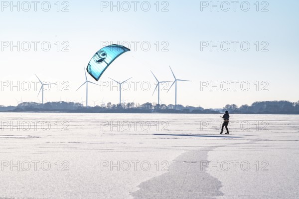 Person kiting on frozen Dümmer Lake, wind turbines in the background, Lembruch, Diepholz district, Lower Saxony, Germany