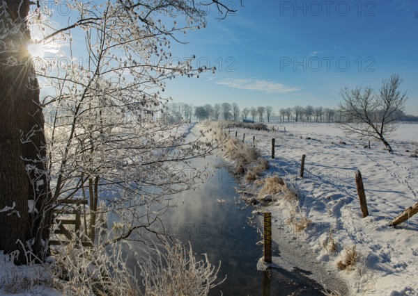 Snowy winter landscape with a small ditch and sunlit trees and fence, Hüde, Dümmer nature park Park, Lower Saxony, Germany