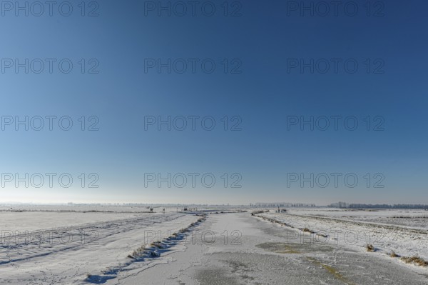 Snowy open landscape with wide sky and distant horizon under blue sky in the foreground the frozen Hunte River just in front of it flows into Dümmer See, Hüde, Dümmer nature park Park, Lower Saxony, Germany