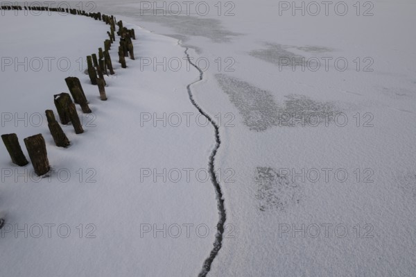 Frozen lake surface of Dümmer See with wooden posts and distinctive fault line in ice, frozen landscape with cracks and barriers on ice under grey sky, Lembruch, Diepholz district, Lower Saxony, Germany