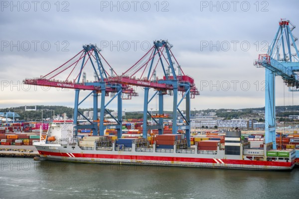 Large port with several blue and red cranes and container ships under cloudy sky, Gothenburg, Västra Götalands län, Sweden