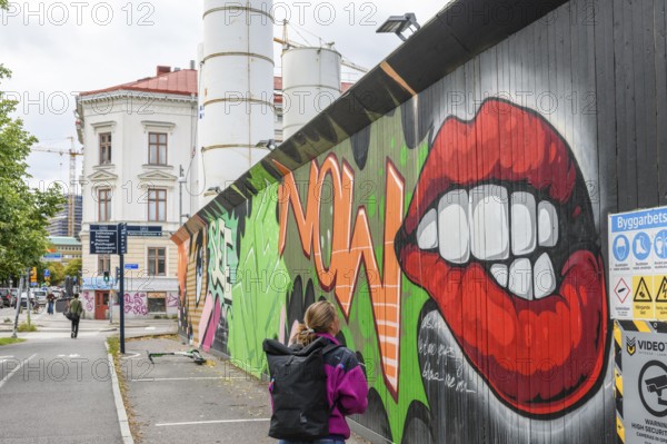 Colourful graffiti on an urban street scene with eye-catching lip motifs is viewed by a young woman, colorful mural street art, Gothenburg, Västra Götalands län, Sweden