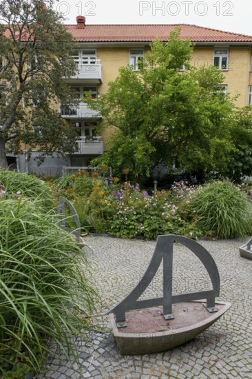 Green garden with art installations and lush plants in front of a residential building, Gothenburg, Västra Götalands län, Sweden