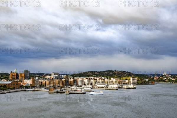 Urban landscape with waterside buildings and hills in the background under cloudy sky, Gothenburg Harbour, Göteborg, Västra Götalands län, Sweden
