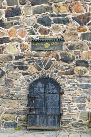 Historic stone wall with a metal door and a sign about Skansen Kronan, detail of an old stone wall in Gothenburg's Skansen Kronan fortress with historic signs, rustic masonry, Gothenburg, Västra Götalands län, Sweden