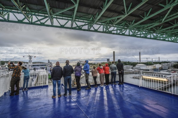 Group of people on a ship deck looking at the harbor crossing under the Älvsborgsbron suspension bridge under a cloudy sky on a ferry boat, Stena Line Gothenburg-Kiel, Gothenburg, Västra Götalands län, Sweden
